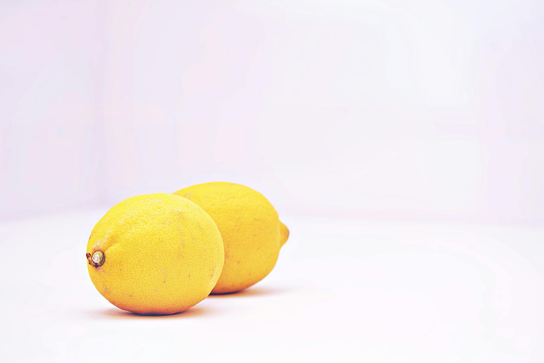 Deux citrons vibrants placés contre un fond blanc minimaliste, symbolisant la fraîcheur et le renouveau après l'arrêt du contraceptif hormonal