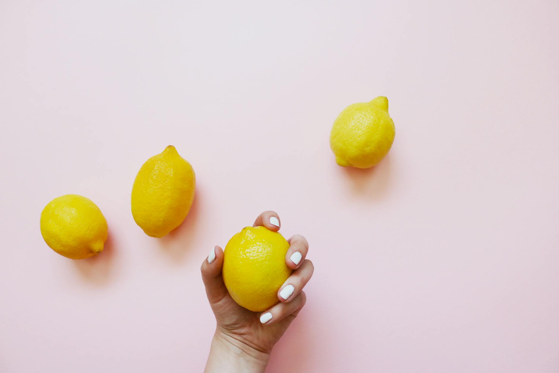 Une main tenant un citron jaune vif sur un fond rose doux avec d'autres citrons autour