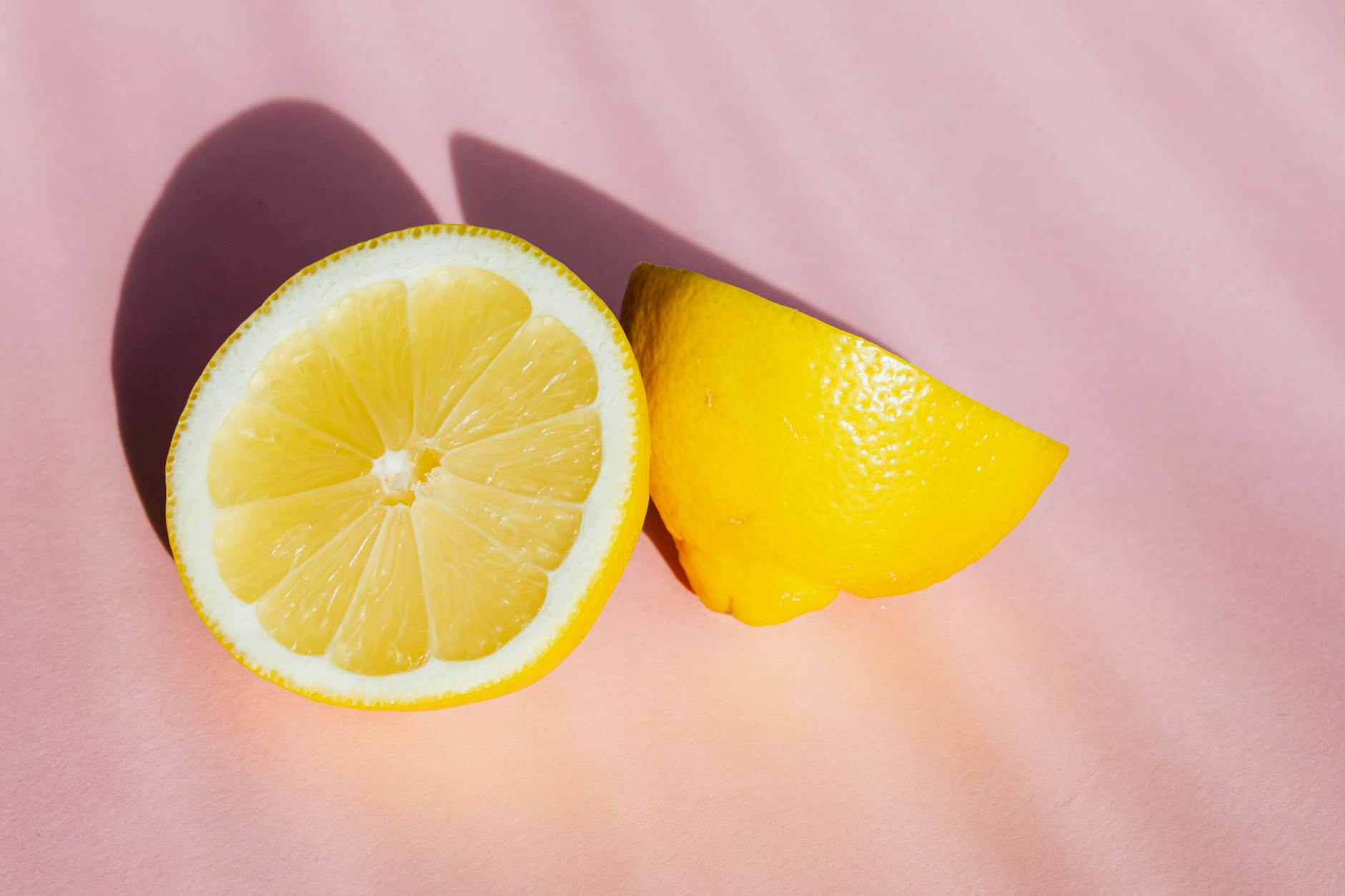 Une main tenant un citron frais sur un fond rose doux, symbolisant la sensualité et la fraîcheur du stimulateur citron