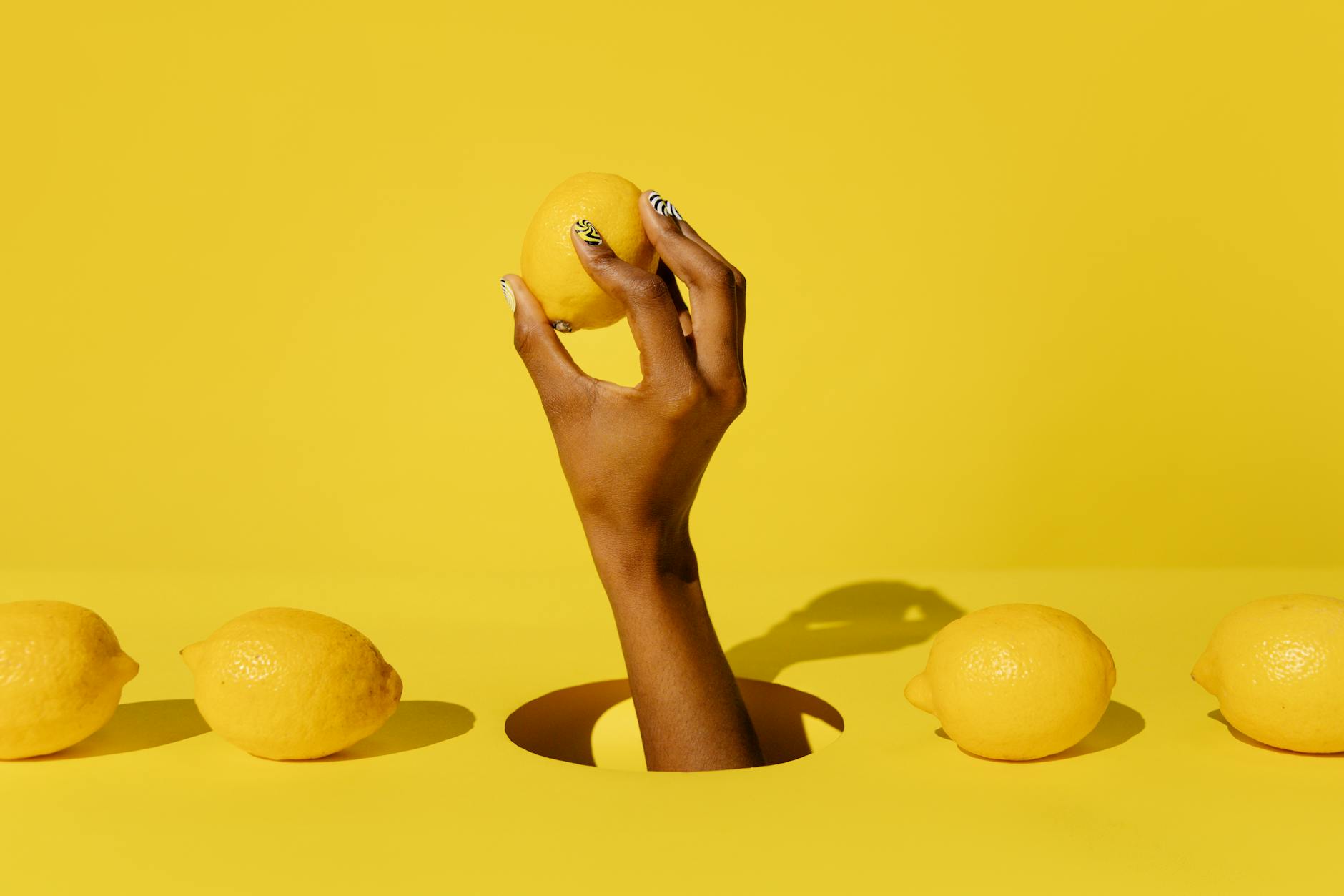 Main tenant un citron frais sur fond jaune vibrant, symbolisant la sensation de fraîcheur et le plaisir sensoriel