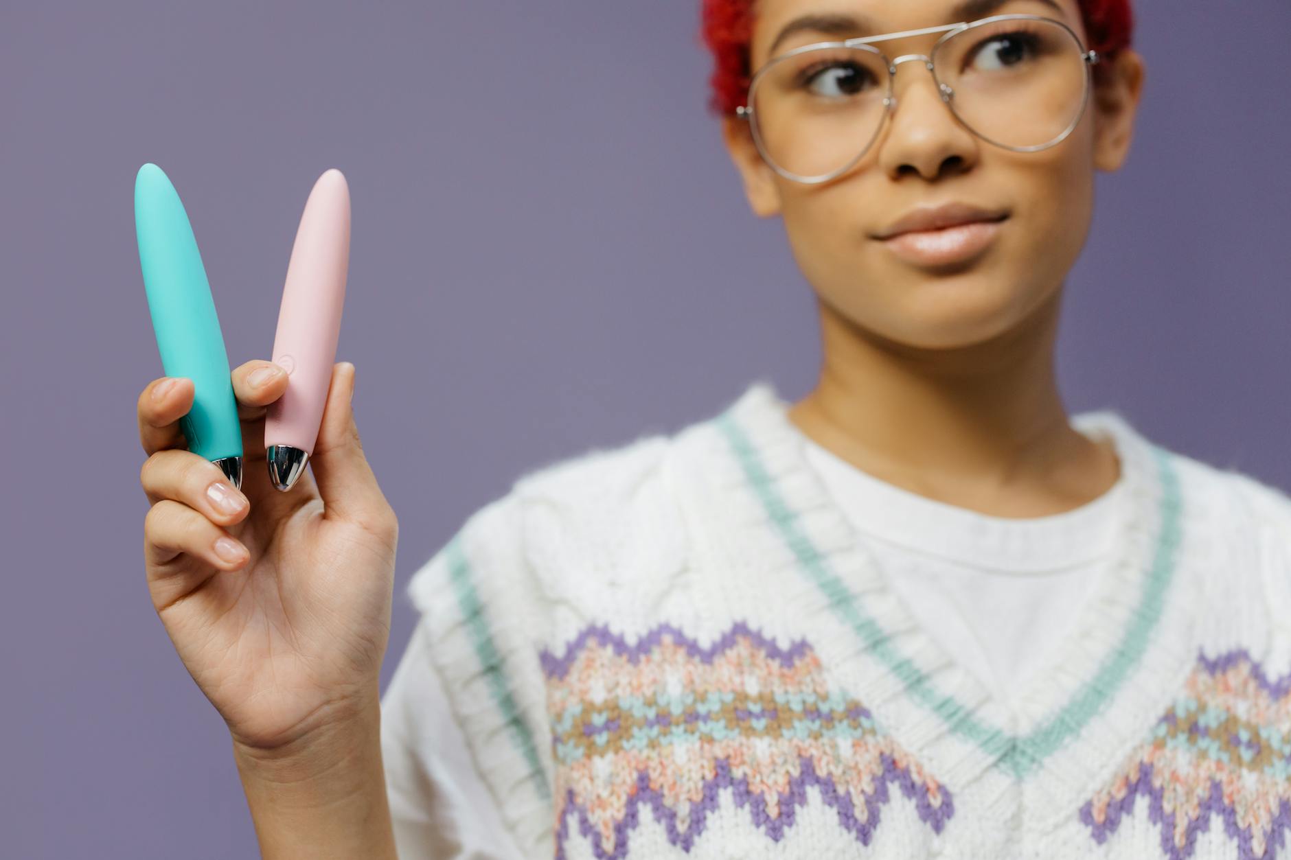 Femme avec lunettes tenant deux vibromasseurs colorés sur fond violet