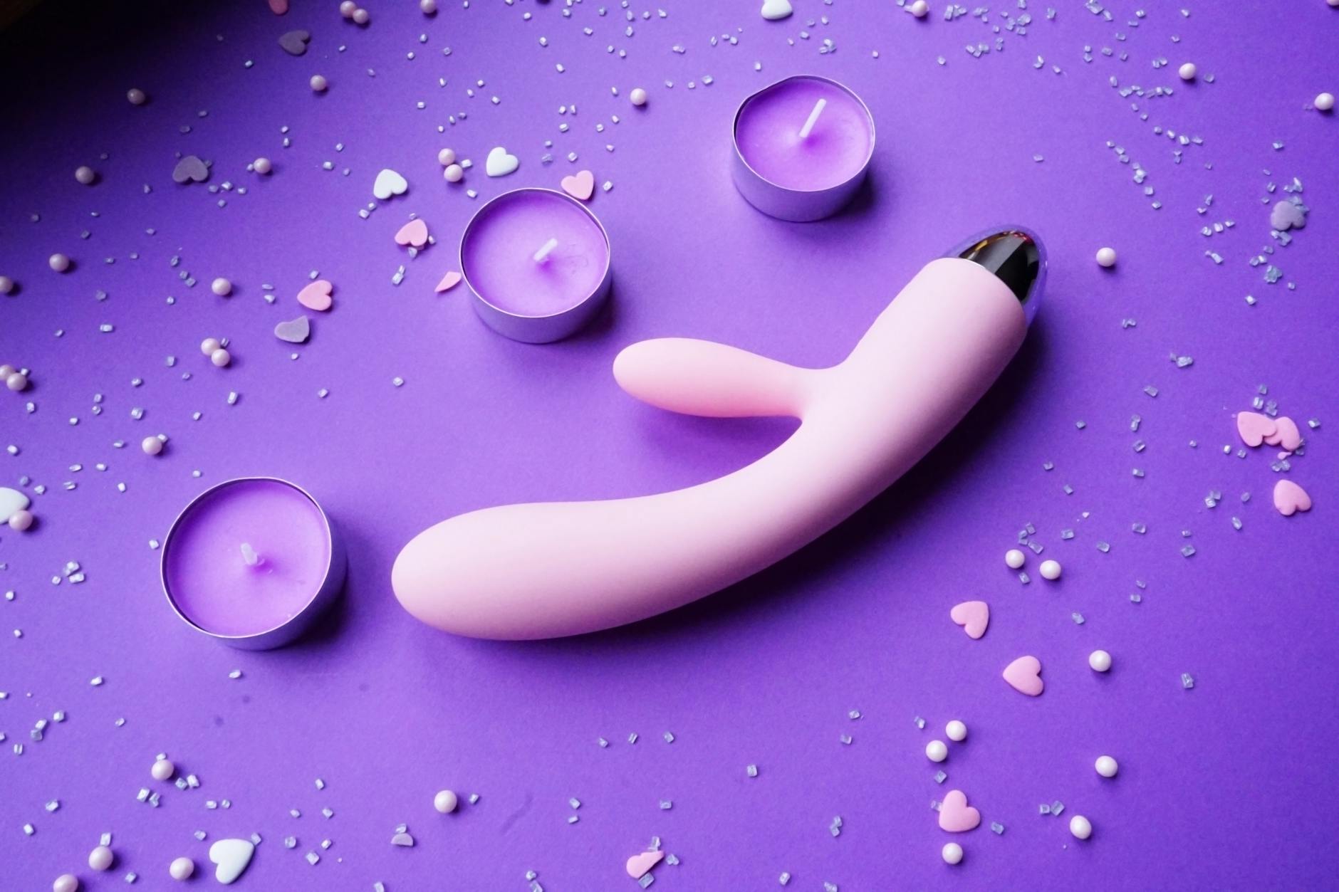 Vibromasseur rose sur fond violet avec confettis cœur et bougies pour une ambiance romantique