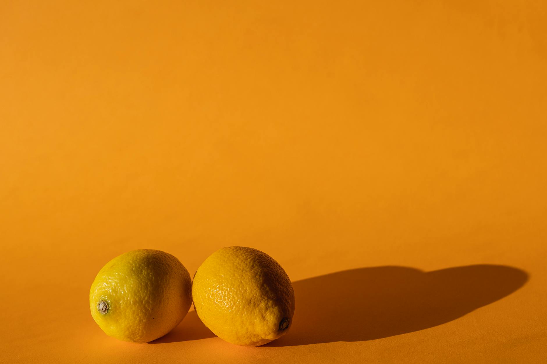 Une main tenant un citron sur fond rose doux, entourée de citrons supplémentaires, symbolisant la fraîcheur et le plaisir